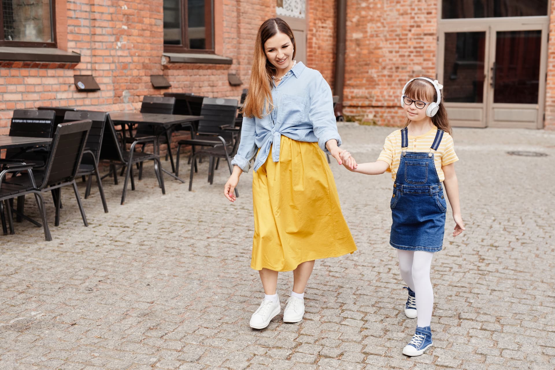 Smiling mother and daughter with Down syndrome holding hands while walking outdoors