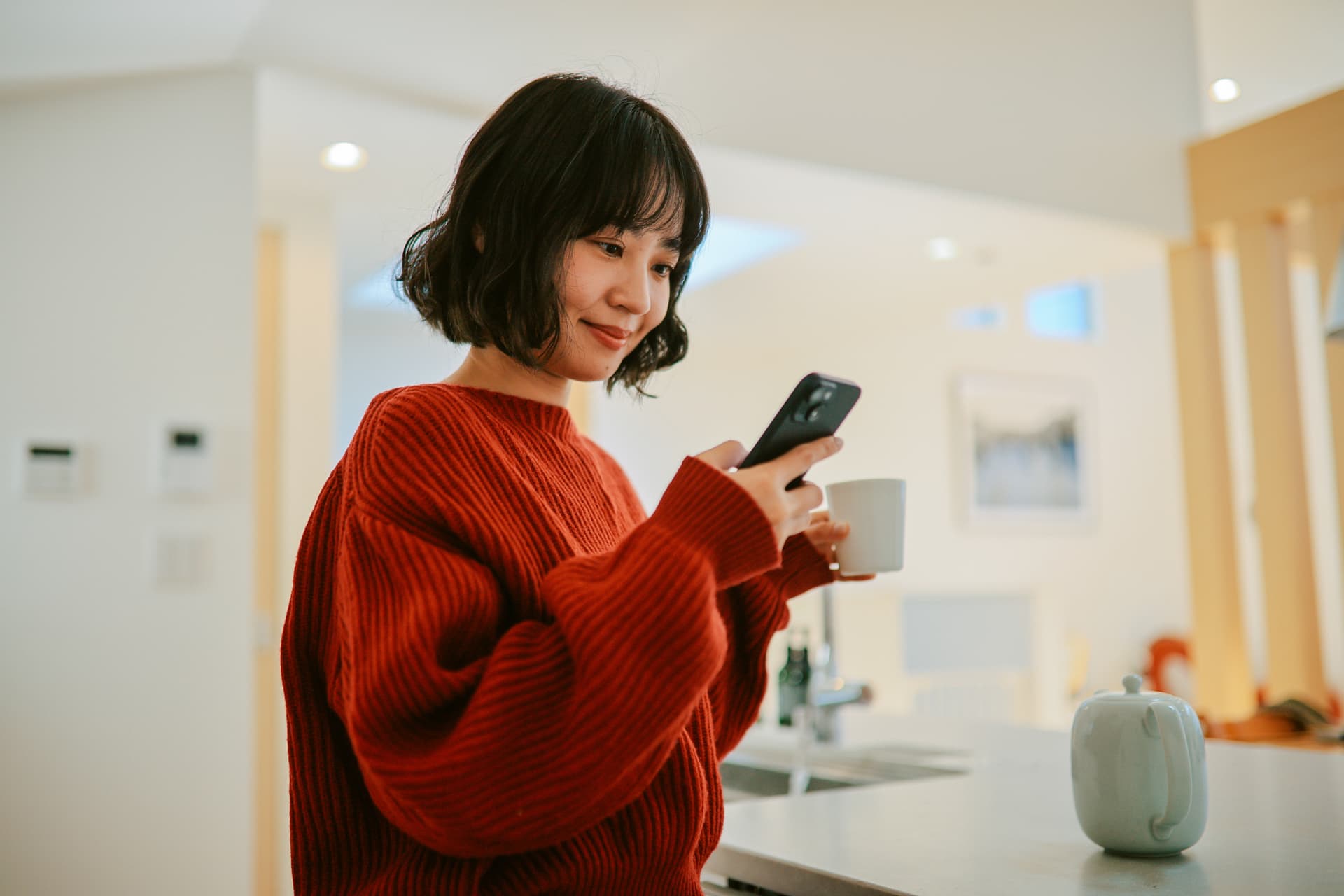 Woman smiling while checking her phone and holding a coffee cup at home