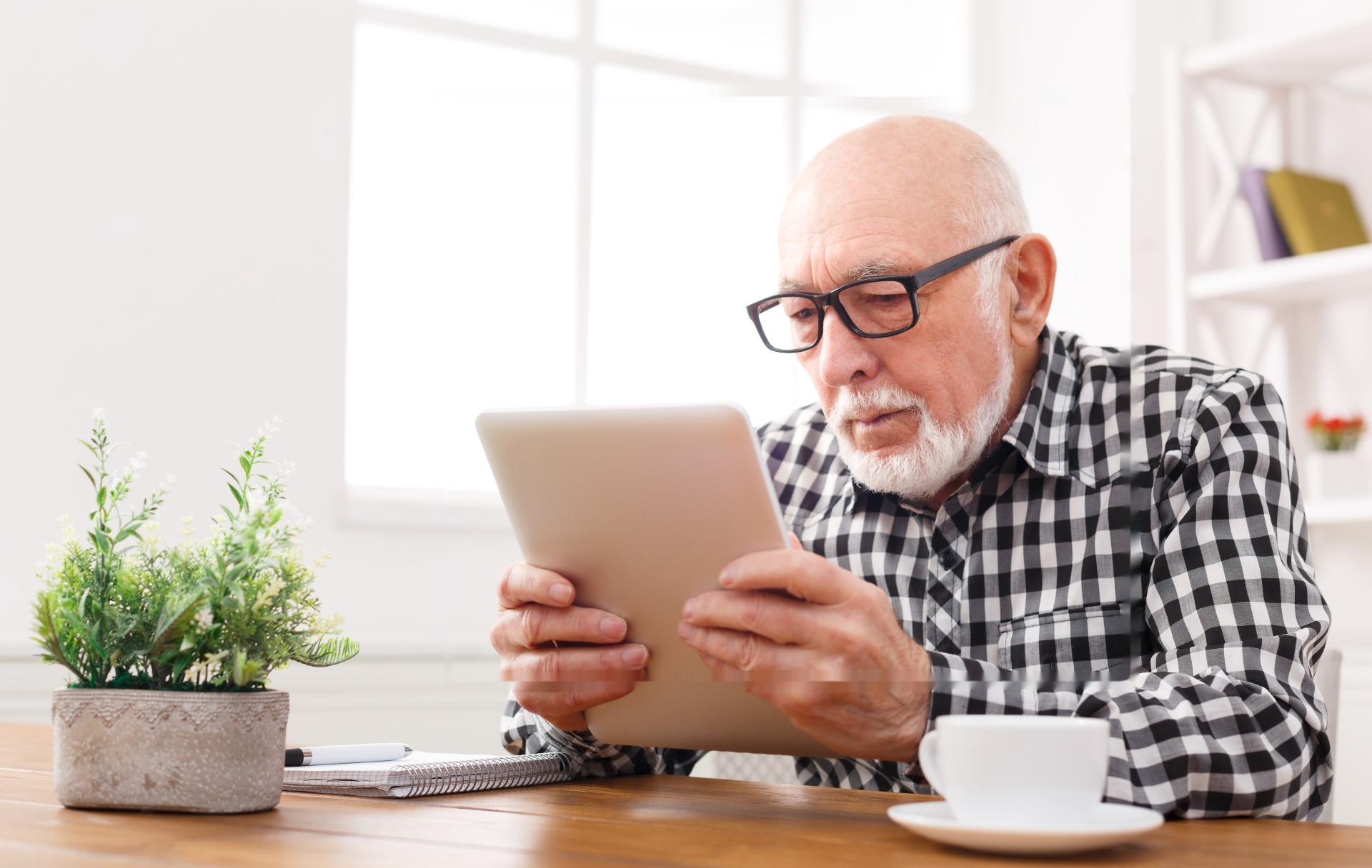 Older man smiling while using a tablet on a couch at home